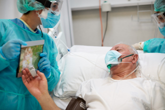 Intensivpflegekräfte zeigen einem COVID-19-Patienten das Foto seiner Enkelin